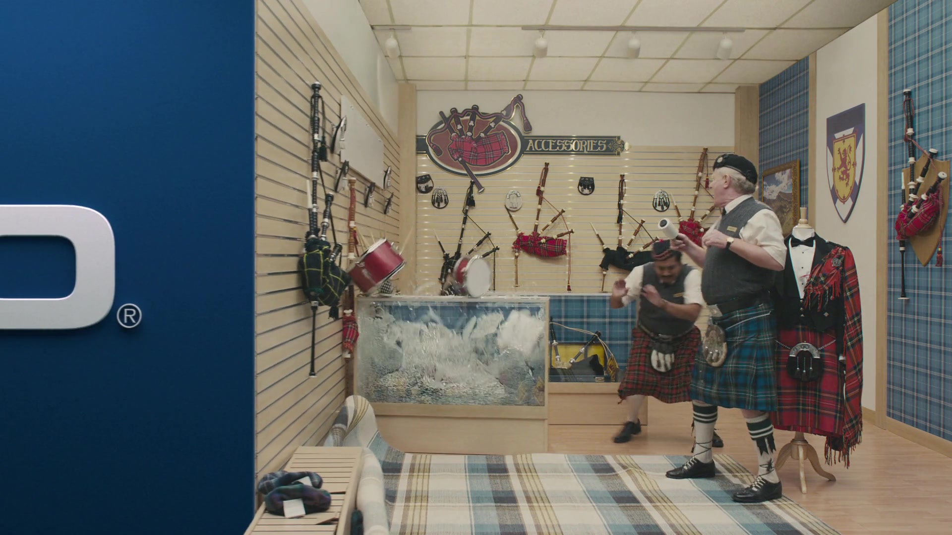 Two kilted men react as a moving blue wall crushes a bagpipe shop and shatters a display case.