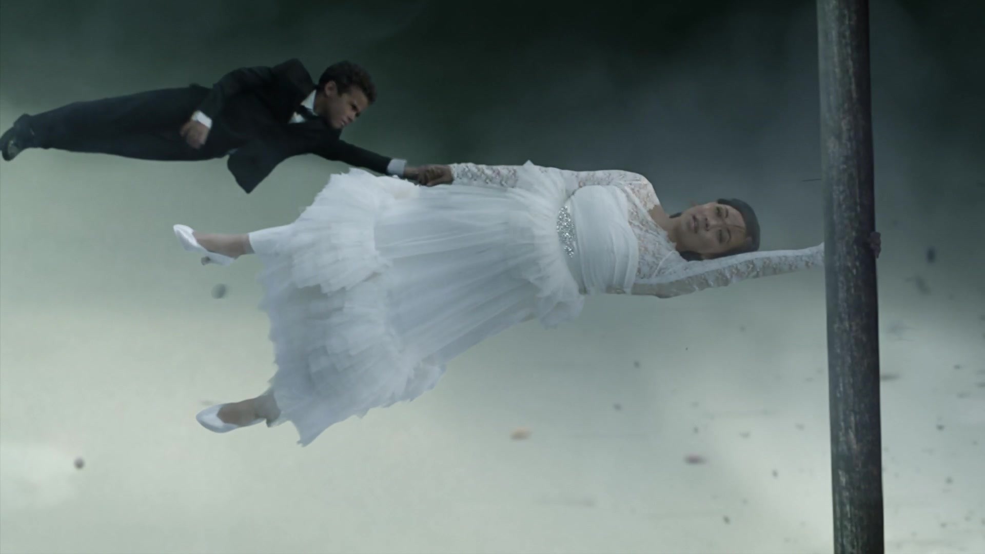 Tornado — Bride holding a pole while groom holds her arm, both horizontal in tornado wind