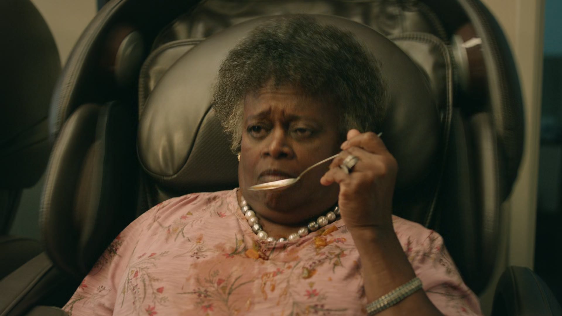 Grandmother struggling to eat from shaking massage chair, spoon raised.